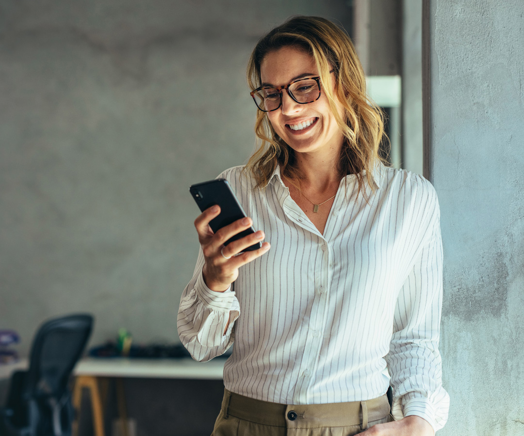 Lächelnde Frau mit Smartphone in der Hand, die eine Nachricht liest – symbolisch für unkomplizierte Kontaktaufnahme mit MicroConsult.